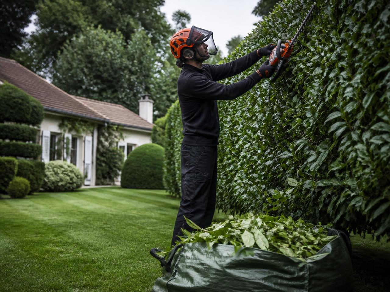 Paysagiste CM.Paysagiste taillant une haie de laurier dans un jardin